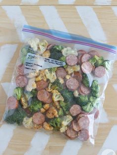 a bag filled with sausage and broccoli sitting on top of a wooden table