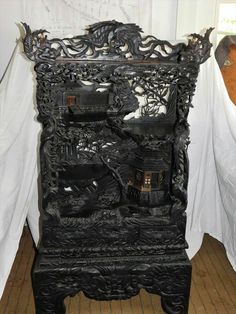 an ornate black wooden cabinet sitting on top of a hard wood floor next to a white curtain