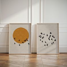 two framed pictures with birds flying in front of an orange and black circle on the wall