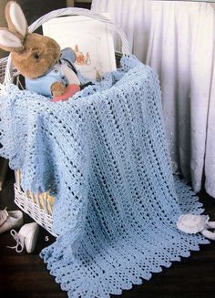 a blue crocheted blanket sitting on top of a basket next to a stuffed animal