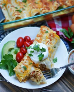 a white plate topped with lasagna next to a bowl of tomatoes and cucumbers