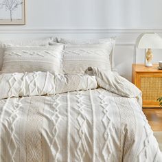 a bed with white comforter and pillows in a room next to a lamp on a table