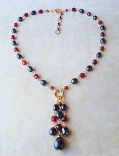 "You really can't go wrong with this classic necklace. It is so elegant and versatile, perfect for all seasons. This lariat style necklace combines luminous baroque black pearl with red garnet crystals. It features a decorative infinity circle plated in 24 karat gold. This necklace measures 16\" in length, with 2 inches extension. The pendant-tassel measures 2\" in length. This stunning necklace is unique, feminine and eye-catching, Perfect for anyone that wants to make a statement or to wear to Elegant Red Lariat Necklaces, Elegant Red Lariat Necklace, Elegant Beaded Dangle Necklaces With Lobster Clasp, Elegant Beaded Dangle Necklace With Lobster Clasp, Elegant Wire Wrapped Dangle Beaded Necklaces, Elegant Red Necklace With Dangling Beads, Elegant Red Wire Wrapped Necklace, Ruby Choker, Lariat Style Necklace