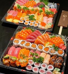 two trays filled with different types of sushi on top of a table next to each other