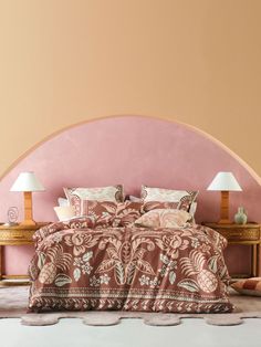 a large bed sitting under a pink wall next to two tables with lamps on them