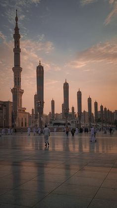 many people are walking around in the middle of an open area with tall buildings behind them