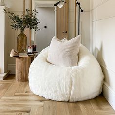 a white bean bag chair sitting on top of a hard wood floor next to a potted plant