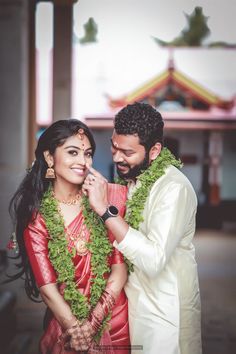 a man and woman standing next to each other in front of a building with green garlands