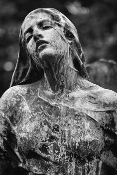 a black and white photo of a statue with its head tilted to the side, in front of trees