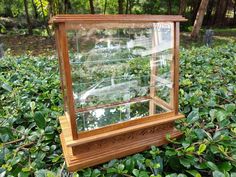 a glass case sitting on top of a lush green field filled with trees and bushes