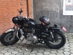 a black motorcycle parked in front of a brick building with a helmet on it's head