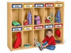 a young boy sitting on the ground in front of a wooden cubby with toys