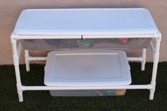 a white table with a plastic tray underneath it on the grass next to a wall