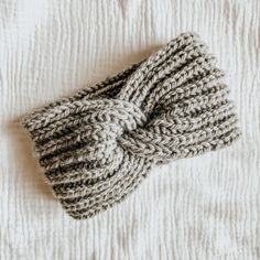 a gray knitted headband laying on top of a white bed sheet with a knot in the middle