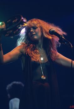 a woman with long red hair holding a microphone in front of her and singing into the microphone