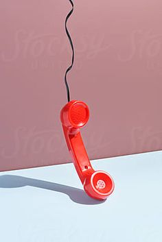 a red telephone sitting on top of a white table next to a pink wall by an electrical cord