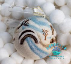 a white and blue ornament sitting on top of cotton balls with trees painted on it