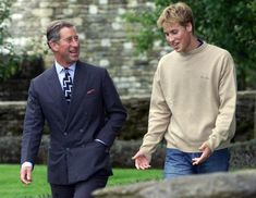 two men in business attire are walking through the grass and talking to each other while one man is wearing a sweater and tie