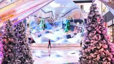 a person standing in front of a giant snow globe at an indoor shopping mall with christmas trees and decorations