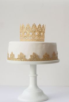 a white cake topped with a gold crown sitting on top of a white tablecloth