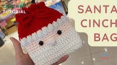 a hand holding up a small crocheted santa clause case in front of a store