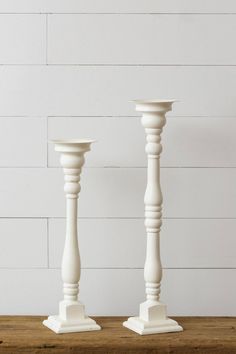 two white candlesticks sitting on top of a wooden table next to each other