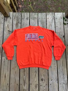 "Show your love for the Florida Gators with this vintage Champion University of Florida Gators Orange Crewneck Sweatshirt. This sweatshirt is made from high-quality materials and features the Gators team logo prominently on the front. Perfect for football season and any Gators fan, this sweatshirt comes in size XL and is made by Tultex. perfect for both men and women. It is also perfect for regular season games and is a must-have for any sports fan. This item is made in Mexico and is perfect for Vintage Graphic Print Sweatshirt For Fan Gear, Vintage Graphic Print Sweatshirt For Fans, Retro Fan Gear Sweatshirt For Fall, Retro Fall Sweatshirt For Fan Gear, Vintage Letter Print Sweatshirt For Fan Gear, 90s Style Long Sleeve Sweatshirt Fan Merchandise, Retro Fall Fan Gear Sweatshirt, Vintage Fan Gear Tops With Crew Neck, Vintage Crew Neck Tops For Fan Gear