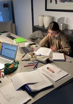 a woman sitting at a desk with papers and laptops on it, looking down