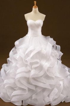 a white wedding dress with ruffles on the skirt and top is shown in front of a mannequin