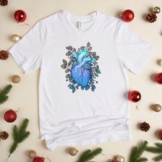 a white t - shirt with a blue heart surrounded by greenery and christmas ornaments