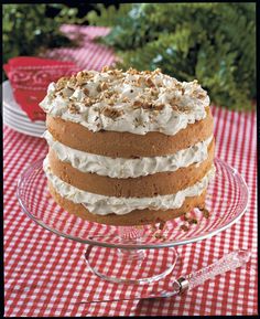 a layered cake with white frosting and walnuts on a red checkered tablecloth