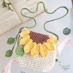 a crocheted sunflower purse sitting on top of a table next to an open book