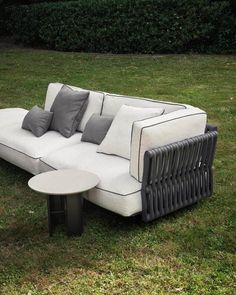 a white couch sitting on top of a lush green field next to a small table