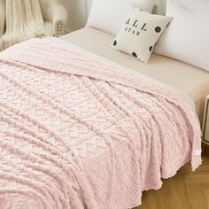 a bed with a pink blanket on top of it next to pillows and a pillow