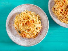 two white bowls filled with spaghetti on top of a blue table