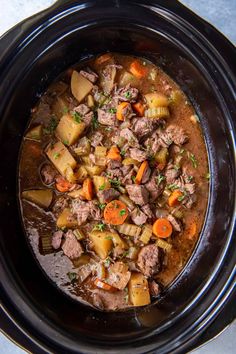 a crock pot filled with beef stew and carrots on top of a table