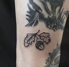 a close up of a person's leg with tattoos on it and an acorn