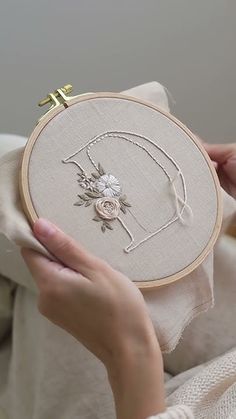 a woman is holding a small embroidered item in front of her face and the embroidery has flowers on it