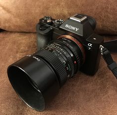 a camera sitting on top of a brown couch next to a black lens with the word sony written on it