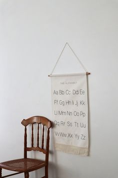 a wooden chair sitting in front of a white wall with a sign hanging on it