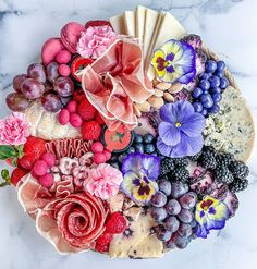 a platter filled with fruit and flowers on top of a marble countertop,