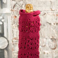 a red crocheted wine bottle holder with a gold top