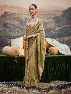 This chic tissue sari is an exquisite embodiment of timeless elegance, featuring delicate dabka work and a gotta patti border adorned with ghumroos. Paired with a chanderi silk blouse embellished with intricate mirror work, this ensemble blends traditional craftsmanship with a modern flair, perfect for elevating your festive look. Gold Pre-draped Saree With Sheer Dupatta For Navratri, Pista Green Pre-draped Saree With Mirror Work For Navratri, Diwali Tissue Silk Sharara With Gota Work, Eid Traditional Wear With Gota Work On Tissue Silk, Transitional Tissue Silk Sharara With Dupatta, Festive Tissue Silk Sharara With Gota Work, Festive Tissue Silk Sharara With Cutdana, Navratri Anarkali Set With Sheer Dupatta In Tussar Silk, Festive Tussar Silk Sharara With Gota Work