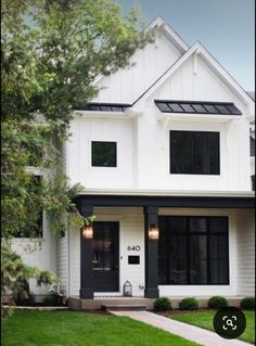 a white house with black trim on the front door and windows, grass in front of it