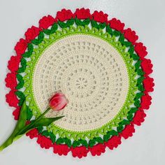 a crocheted doily with a red flower on the center and green border