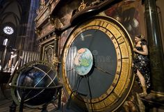 a woman standing next to a large clock in a building with an earth globe on it