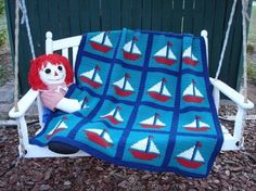 a teddy bear is sitting on a swing next to a crocheted blanket that has sailboats on it