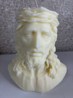 a white candle with a statue of jesus on it's face in front of a wall