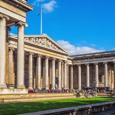 an old building with columns and people sitting on the grass in front of it,