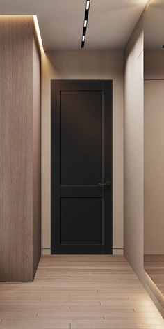 an empty room with a black door and wooden flooring is lit by recessed lights